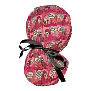May include: A pink scrub cap featuring a repeating comic book style print of a masked character in a robe. The text bubbles contain the phrases Very Demure, Very Mindful, Very Scary, and Did you see how I chased them. A black ribbon is tied at the back.