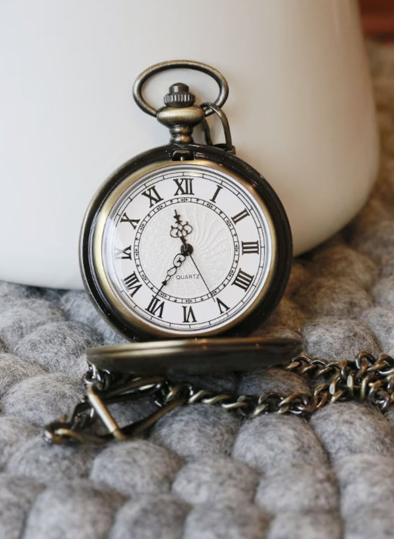 K&ouml;nnte beinhalten: Antike bronzefarbene Taschenuhr mit wei&szlig;em Zifferblatt und schwarzen r&ouml;mischen Ziffern. Die Uhr hat eine Kette und ist teilweise ge&ouml;ffnet, wodurch die Zeit sichtbar wird. Das Wort "QUARTZ" ist auf dem Zifferblatt aufgedruckt.