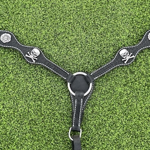 May include: Black horse breast collar with silver skull and rose accents. The collar has a wavy design with white stitching. The background is green.