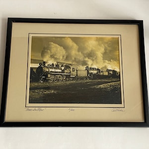 May include: A framed black and white photograph of a steam train with smoke billowing from the engine. The train is moving through a rural landscape. The photograph is signed "Three-in-Row" and "Carl Price".