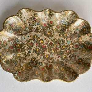 May include: A decorative, scalloped, oval-shaped tray with a gold rim and a colorful floral pattern. The tray is made of paper mache and has a vintage look.