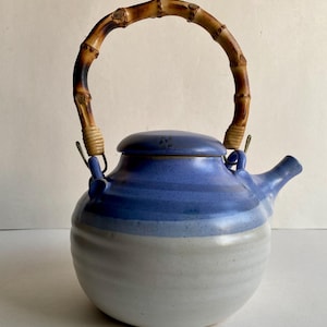 May include: A blue and white ceramic teapot with a bamboo handle. The teapot has a rounded body and a lid with a knob.