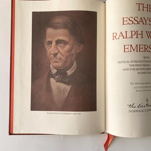 Puede incluir: Un libro abierto con un retrato de Ralph Waldo Emerson en la p&aacute;gina izquierda. La p&aacute;gina derecha presenta texto rojo que dice "The Essays of Ralph Waldo Emerson". Una cinta roja como marcador de libro es visible. El libro est&aacute; encuadernado en una cubierta roja oscura.