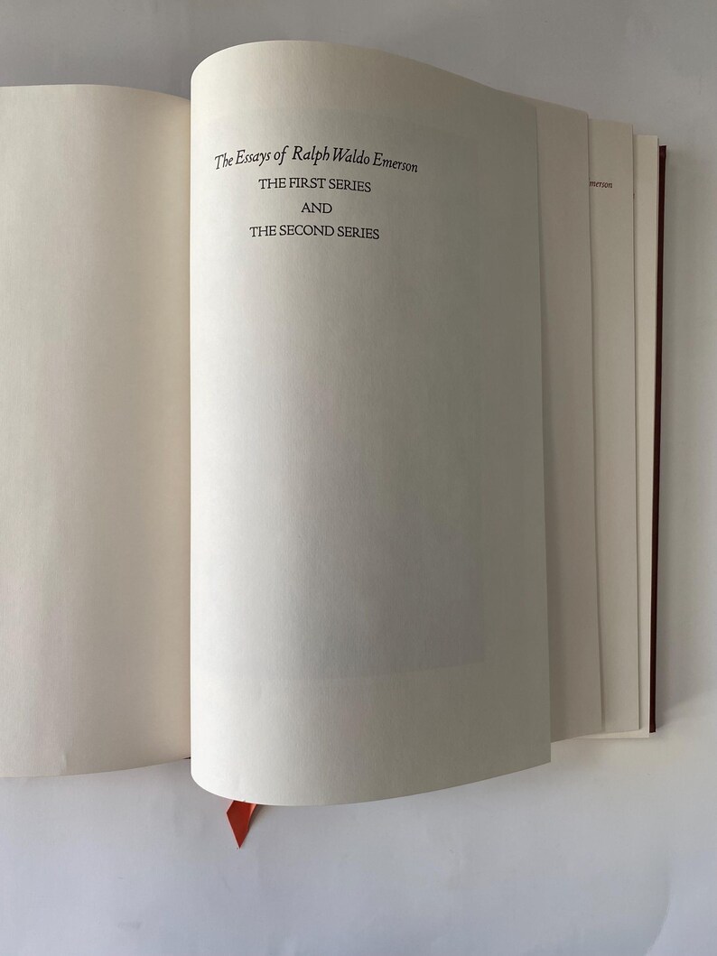 Puede incluir: Libro abierto con el t&iacute;tulo "The Essays of Ralph Waldo Emerson" impreso en la p&aacute;gina derecha. El texto dice "THE FIRST SERIES AND THE SECOND SERIES." Una cinta roja de marcador es visible.