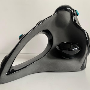 May include: Abstract ceramic sculpture in shades of gray and black, featuring a curved, open design. Accented with small, turquoise-colored embellishments. Includes a small, black, bowl-shaped element. A modern, artistic home decor item.