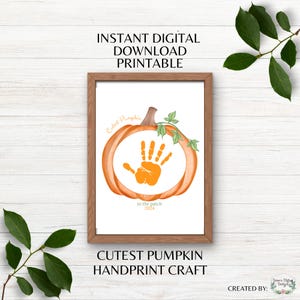 Puede incluir: Una impresión enmarcada con un diseño de calabaza naranja y una huella de mano en el centro. El texto dice "Cutest Pumpkin Handprint Craft" y "Instant Digital Download Printable."