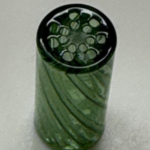 May include: A cylindrical, green glass object with a spiral design. The top features a pattern of small, circular indentations. The glass has a slight transparency, allowing some light to pass through. The object is likely a decorative piece or a component of a larger item.