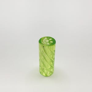 May include: A tall, cylindrical, lime green glass object with a textured, swirling pattern. The top of the object has a dotted design. The glass is transparent, allowing light to pass through. The object is likely a decorative vase or container.