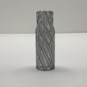 May include: A gray glass vase with a spiral design. The vase is cylindrical and has a textured surface with vertical, swirling lines. The glass appears to be transparent, allowing light to pass through.