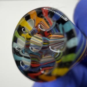 May include: A colorful glass object with a rounded shape, featuring a mix of vibrant colors including yellow, orange, blue, and black. The glass has a textured appearance with several circular indentations, creating a unique visual effect.
