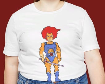 May include: White t-shirt with a cartoon image of Lion-O from ThunderCats. He is wearing a blue and purple costume and holding a sword.