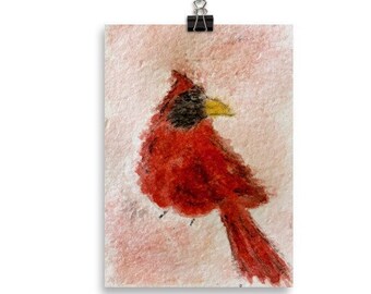 May include: A watercolor painting of a red cardinal bird with a black head and a yellow beak. The bird is perched on a branch and is looking to the right. The background is a light pink color.