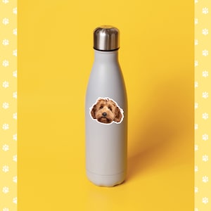 May include: A gray stainless steel water bottle with a sticker of a brown dog's face on it. The bottle is on a yellow background.