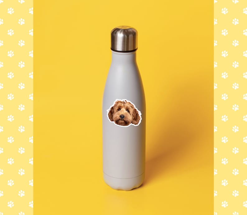 May include: A gray stainless steel water bottle with a sticker of a brown dog's face on it. The bottle is on a yellow background.