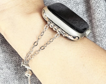 May include: Silver-toned watch band with a chain-link design. The band is attached to a silver watch with a black screen. The watch is on a wrist, and the background is a gray sweater.