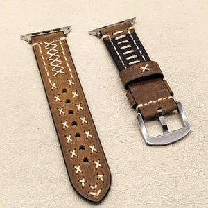 Op de afbeelding: Twee bruine leren horlogebandjes met witte stiksels. E&eacute;n bandje heeft een metalen gesp en het andere een eenvoudige lus sluiting.