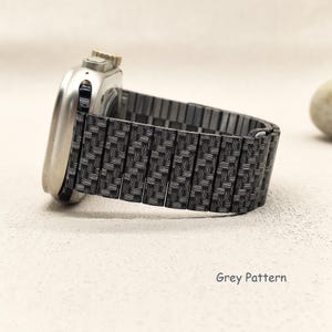 May include: A silver-toned smartwatch with a metallic link watch band featuring a dark grey woven carbon fiber pattern. The watch band consists of rectangular segments connected in a flexible design. The text Grey Pattern is visible.