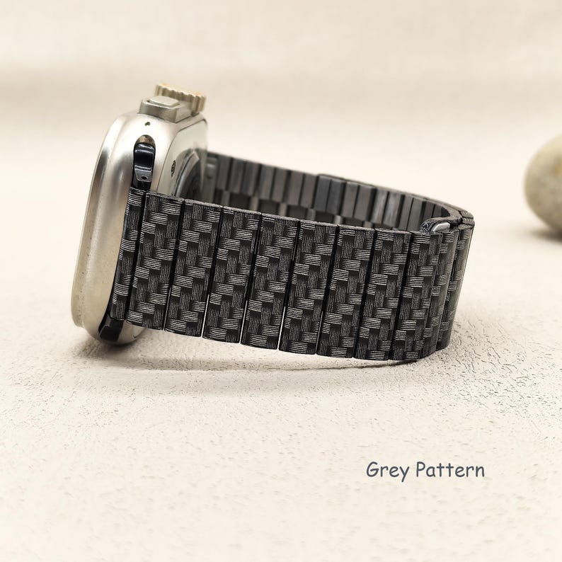 May include: A silver-toned smartwatch with a metallic link watch band featuring a dark grey woven carbon fiber pattern. The watch band consists of rectangular segments connected in a flexible design. The text Grey Pattern is visible.