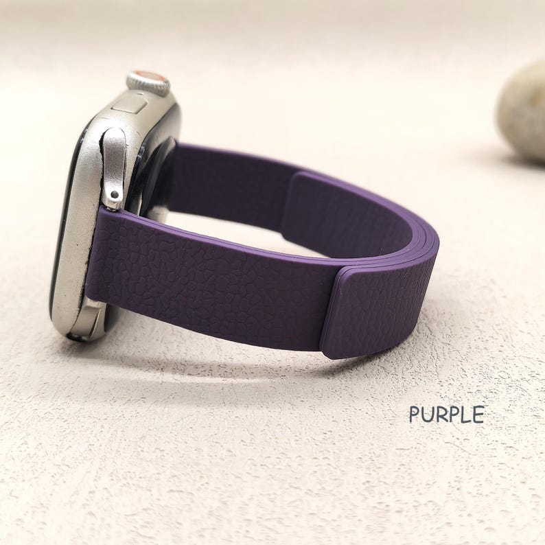 May include: A silver smartwatch with a purple leather band. The band is a solid color with a textured surface. The word "PURPLE" is printed in white on the surface.