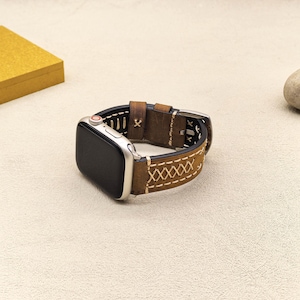 Op de afbeelding: Een bruin leren horlogebandje met witte stiksels voor een Apple Watch. Het bandje heeft een gestikt ontwerp en een gespsluiting.