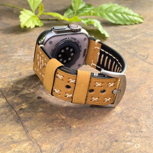 Op de afbeelding: Tan lederen horlogeband met witte stiksels en een roestvrijstalen gesp. Het band is ontworpen voor een Apple Watch met een keramische behuizing.