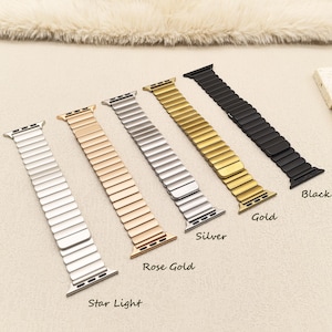 May include: Five metal watch bands arranged in a row, featuring a flexible link design. The colors from left to right are labeled as Star Light, Rose Gold, Silver, Gold, and Black. Each band includes integrated connectors for attachment to a watch.