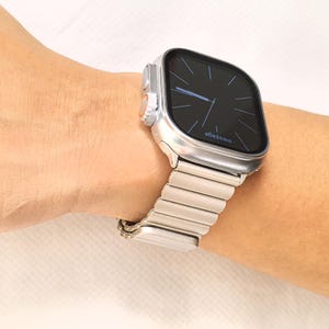 May include: A silver Apple Watch with a silver metal band. The watch face is black with white text that reads "message".