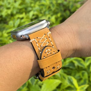 Op de afbeelding: Een tan lederen horlogeband met witte stiksels en een decoratief patroon. De band is ontworpen voor een smartwatch.