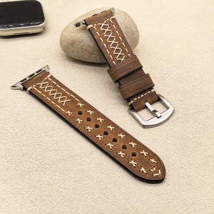 Op de afbeelding: Twee bruine leren horlogebandjes met witte stiksels. De bandjes hebben een kruissteekpatroon en zijn ontworpen voor Apple Watches.