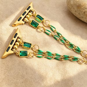 Peut inclure: Bracelet de montre doré avec des pierres précieuses rectangulaires vert émeraude et des maillons de chaîne en émail vert. Le bracelet comporte un connecteur doré avec des accents noirs et de petites perles dorées. Pour Apple Watch.