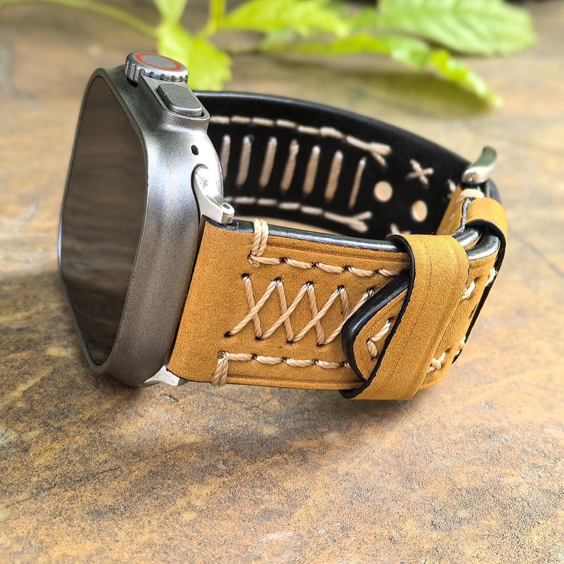 Op de afbeelding: Een tan lederen horlogeband met witte stiksels en een zwarte lederen achterkant. De band is bevestigd aan een zilveren smartwatch.