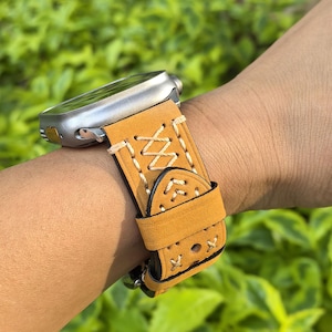 Może przedstawiać: Brązowy skórzany pasek do zegarka z białymi szwami i ozdobnym wzorem. Pasek jest przeznaczony do smartwatcha.