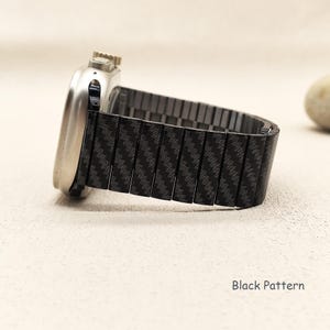 May include: A silver-toned smartwatch with a metallic casing and a black watch band featuring a repeating diagonal carbon fiber-style pattern. The side of the watch displays a crown and button. The text Black Pattern is visible in the corner.