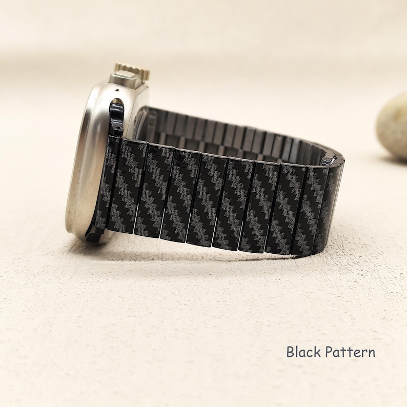 May include: A silver-toned smartwatch with a metallic casing and a black watch band featuring a repeating diagonal carbon fiber-style pattern. The side of the watch displays a crown and button. The text Black Pattern is visible in the corner.