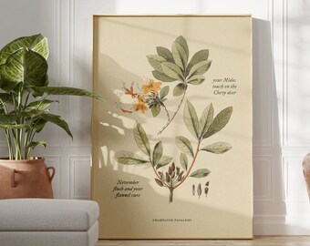 May include: A framed botanical illustration of a plant with green leaves and yellow flowers. The text on the print reads "November flush and your flannel sun" and "your Midas touch on the Cherry door". The print is hanging on a white wall in a room with a potted plant and a white ottoman.