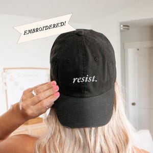 May include: Black baseball cap with the word "resist" embroidered in white on the front.