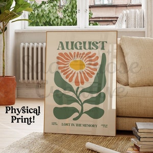 Op de afbeelding: Een vintage poster met het woord "AUGUSTUS" in vetgedrukte groene letters. De poster toont een gestileerde illustratie van een bloem met oranje en roze bloemblaadjes en groene bladeren. De tekst "VERLOREN IN DE HERINNERING" is onder de bloem gedrukt.
