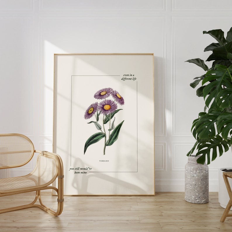 May include: A framed print with a botanical illustration of purple flowers with yellow centers. The text "even in a different life you still would've been mine" and "TIMELESS" are printed below the illustration.
