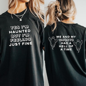 May include: Black t-shirt with white text that reads "Yes I'm Haunted But I'm Feeling Just Fine" on the front and "Me and My Ghosts Had a Hell of a Time" with two ghost illustrations on the back.
