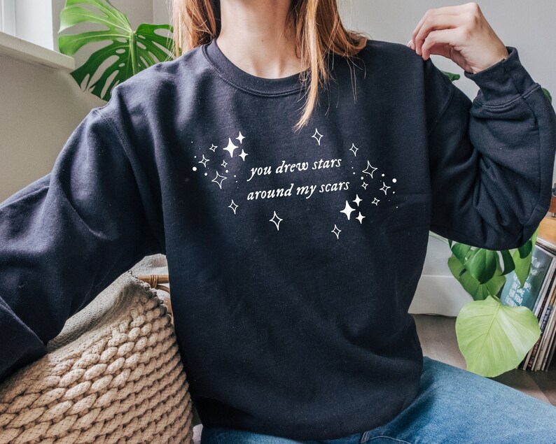 May include: Black sweatshirt with white text that reads "you drew stars around my scars" and a design of white stars.