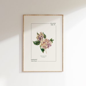 Op de afbeelding: Ingelijste kunstafdruk met een aquarel illustratie van paarse en witte hortensia's. De afdruk bevat tekst: "running back home to you", "FRESH OUT THE SLAMMER", en "now, pretty baby, I'm". De lijst is van licht hout.