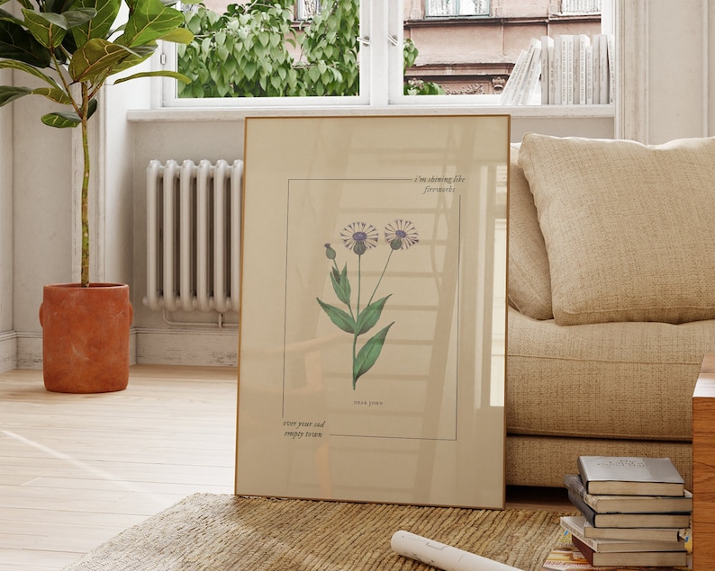 May include: A framed botanical print with a light brown background featuring a purple flower with green leaves. The text on the print reads "I'm showing life fireworks" and "over year and empty room".