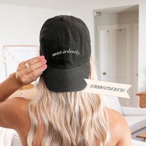 May include: Black baseball cap with the text "most ardently." embroidered in white on the back. EMBROIDERED! is written on a white banner.