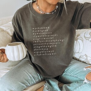 K&ouml;nnte beinhalten: Ein dunkelgraues T-Shirt mit einem wei&szlig;en Grafikdruck eines Wortsuchr&auml;tsels. Das R&auml;tsel enth&auml;lt die W&ouml;rter "wysbswwmd", "dyswaguo", "wywabwyascs", "wywatbdaycwdi", "iffywatbdaycwdi", "aisgrciwsoiwf", "iwdfysiddiaydpbbywgt", "ysiiasttbbycmpayrc", "ysngwbbywgbtm", "ykotbysp", "aipssyhb yawyd", "aifybinftsmwel".