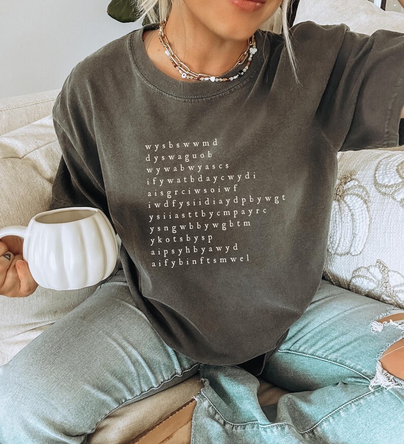 K&ouml;nnte beinhalten: Ein dunkelgraues T-Shirt mit einem wei&szlig;en Grafikdruck eines Wortsuchr&auml;tsels. Das R&auml;tsel enth&auml;lt die W&ouml;rter "wysbswwmd", "dyswaguo", "wywabwyascs", "wywatbdaycwdi", "iffywatbdaycwdi", "aisgrciwsoiwf", "iwdfysiddiaydpbbywgt", "ysiiasttbbycmpayrc", "ysngwbbywgbtm", "ykotbysp", "aipssyhb yawyd", "aifybinftsmwel".