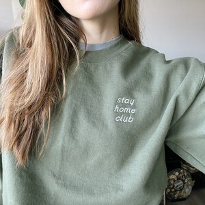 May include: A green sweatshirt with the text "stay home club" embroidered on the front.