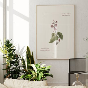 May include: A framed print with a botanical illustration of a pink flower with green leaves. The print has the text "never be so clever you forget to be kind" written in cursive.