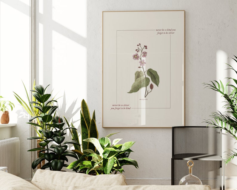 May include: A framed print with a botanical illustration of a pink flower with green leaves. The print has the text "never be so clever you forget to be kind" written in cursive.