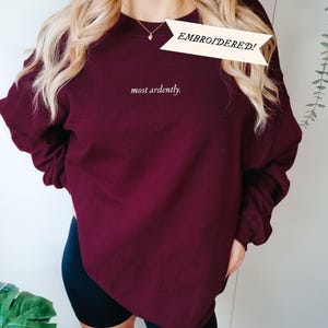 Puede incluir: Sudadera burdeos con el texto bordado "most ardently". Una pancarta sobre el texto dice "&iexcl;BORDADO!". La sudadera es de color liso y tiene mangas largas. La modelo lleva un pantal&oacute;n corto negro.