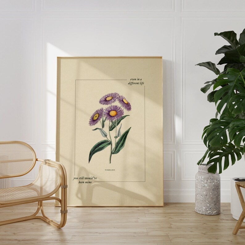 May include: A beige poster with a botanical illustration of purple flowers with yellow centers. The text "even in a different life you still would've been mine" and "TIMELESS" are printed below the illustration.